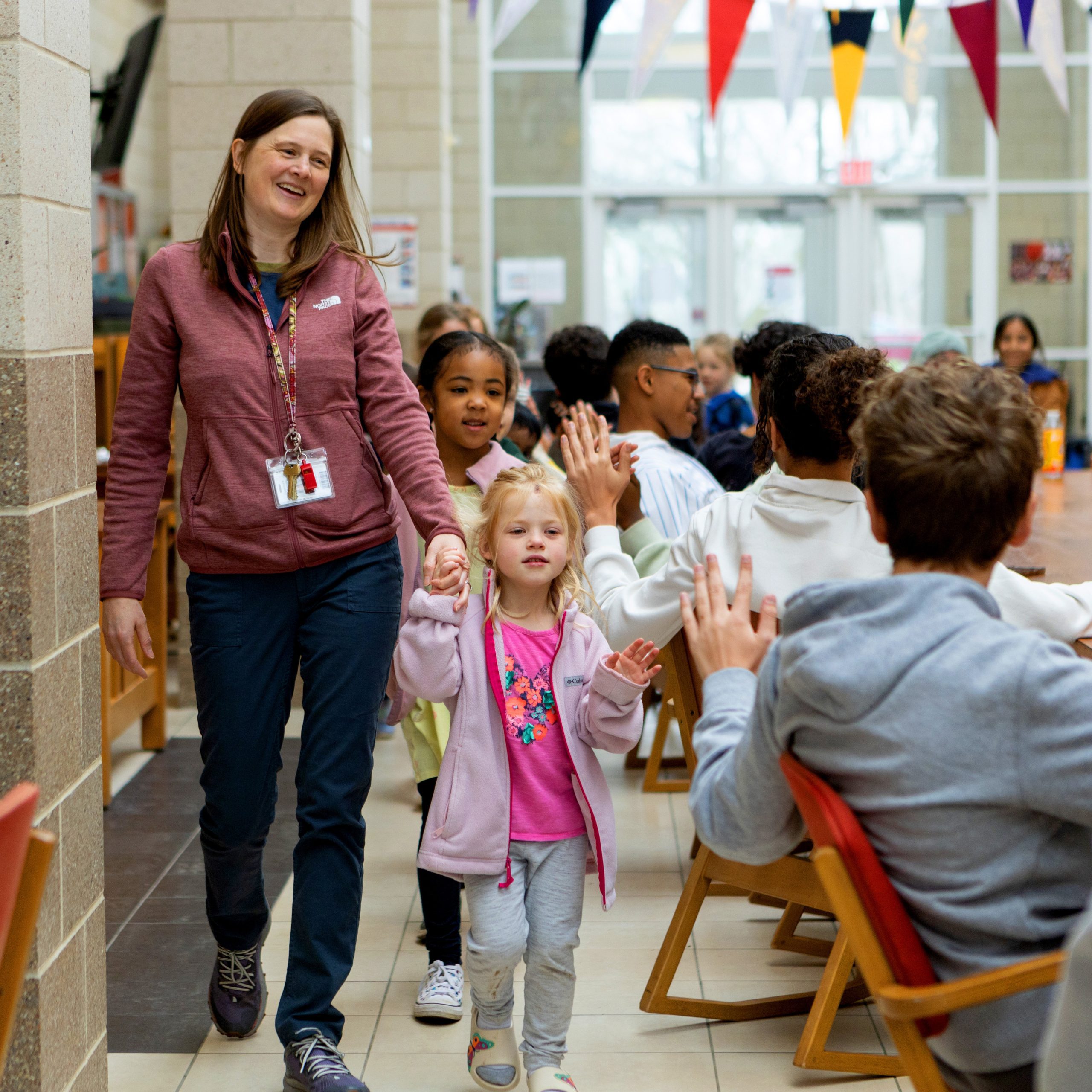 Younger students and their teacher walk down Central Hall and high-five older students.