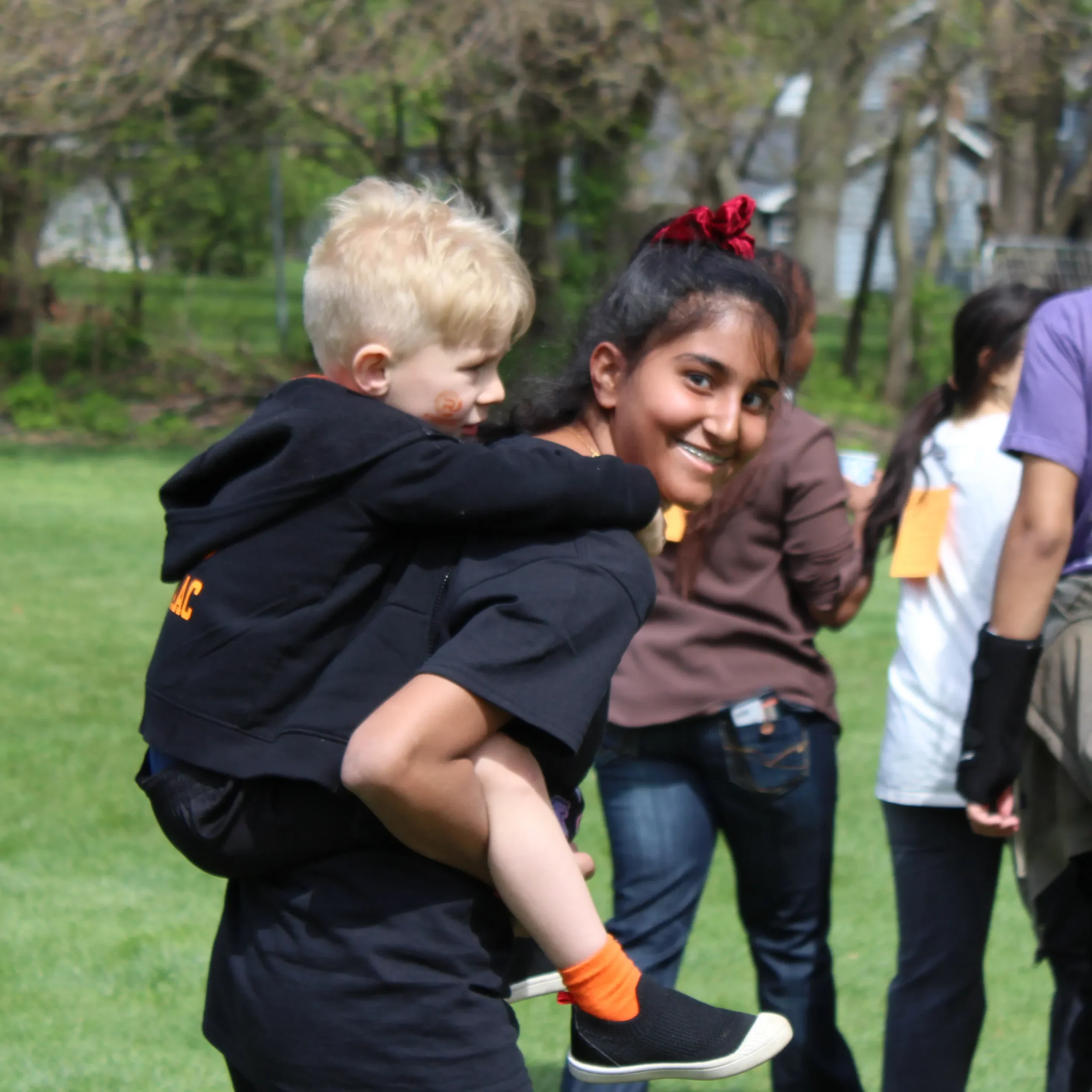 A middle school student carries a younger student on her back. 